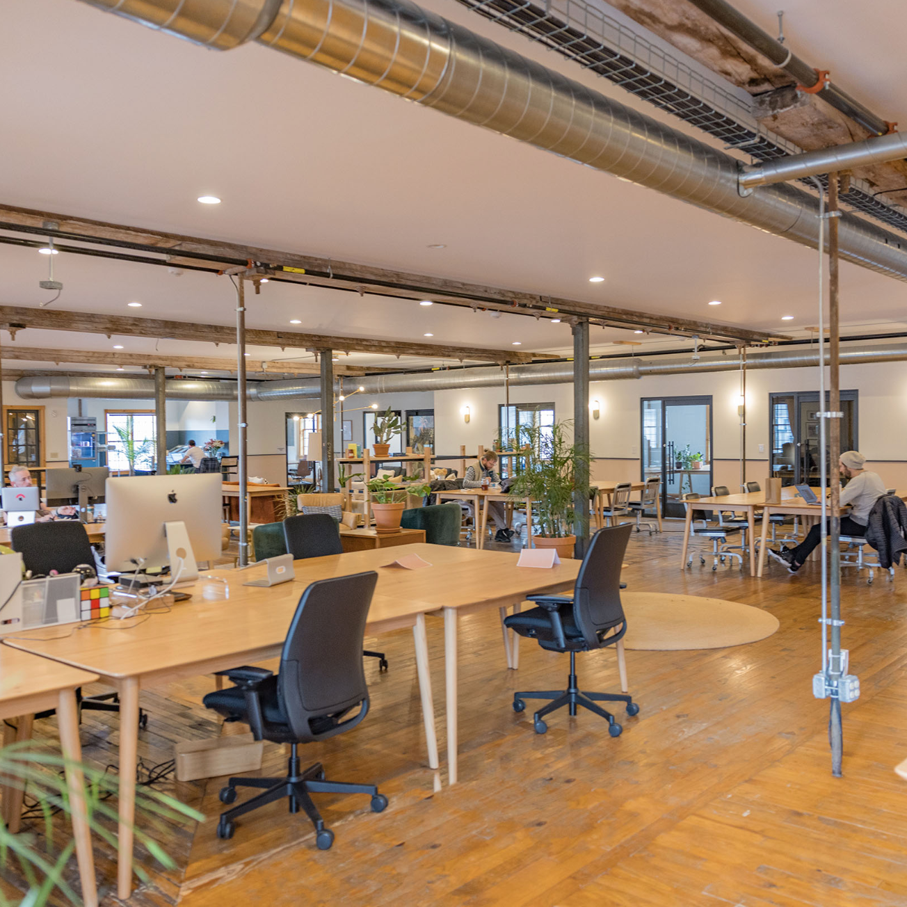 Modern office space with wooden desks, chairs, and large windows.