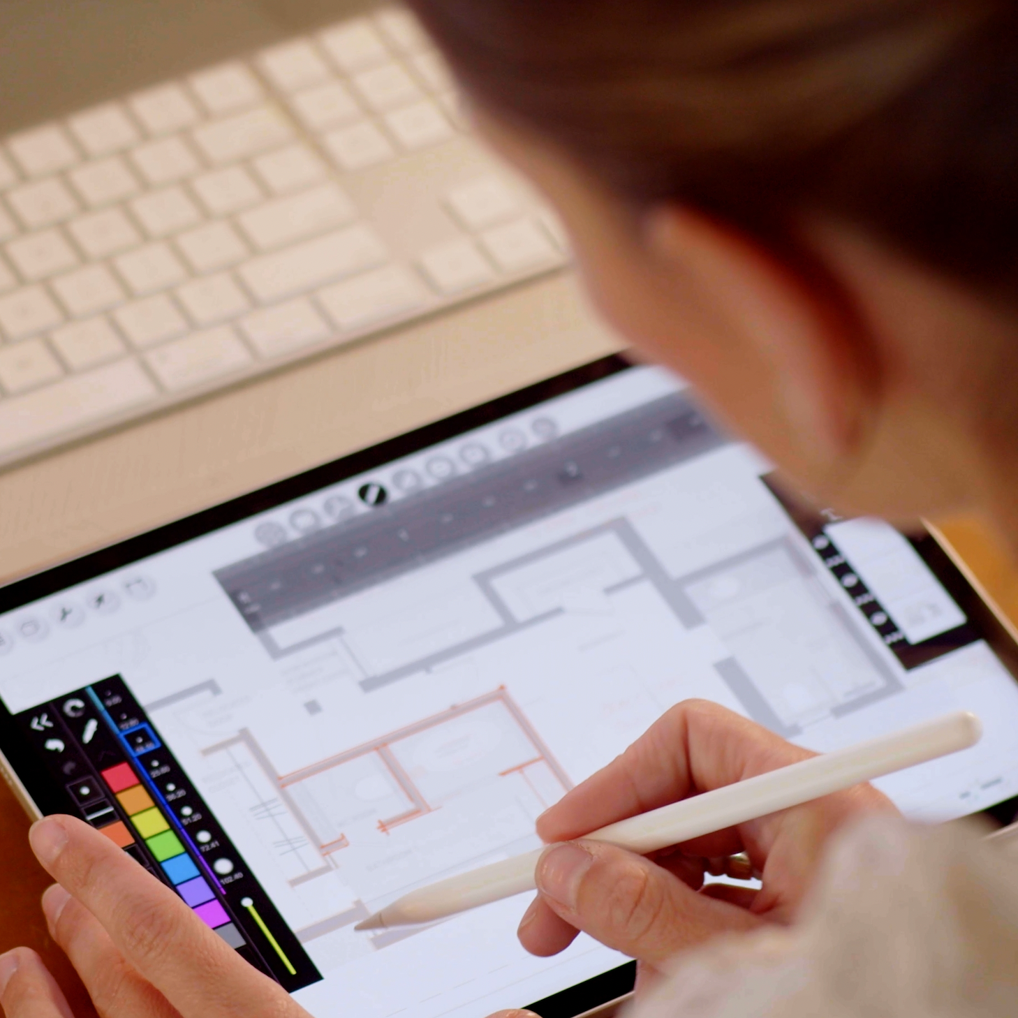 Person using a stylus on a digital tablet with a design app open, next to a laptop.